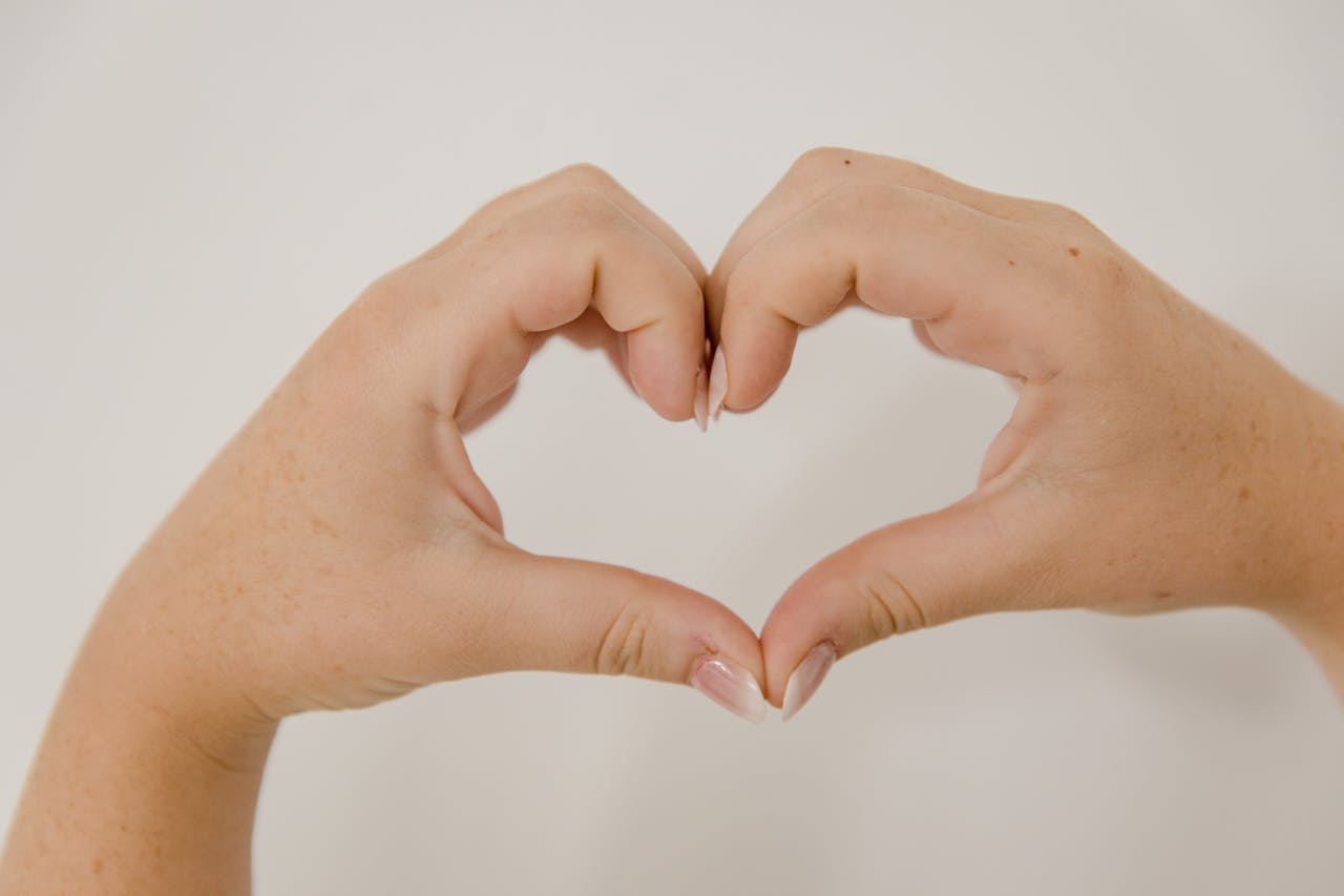 How we can help Close-up of hands making a heart shape on a neutral background, symbolizing love and connection.